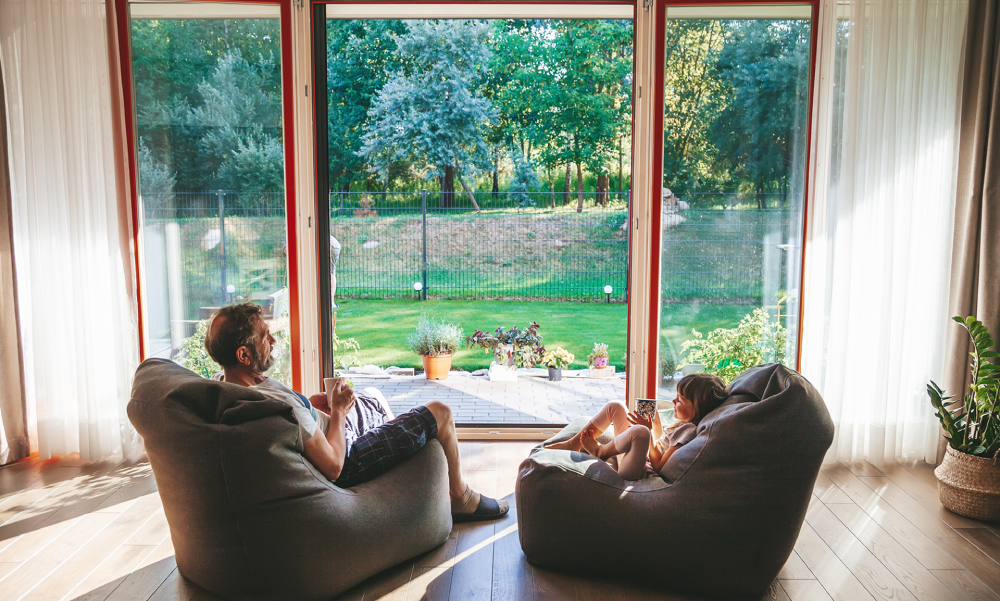 Two people relaxing indoors by large window.